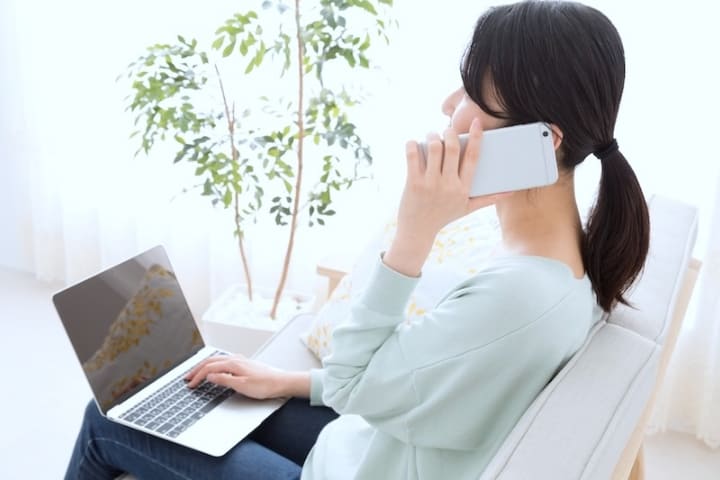 物件確認をイメージする、スマートフォンとノートパソコンで作業する女性