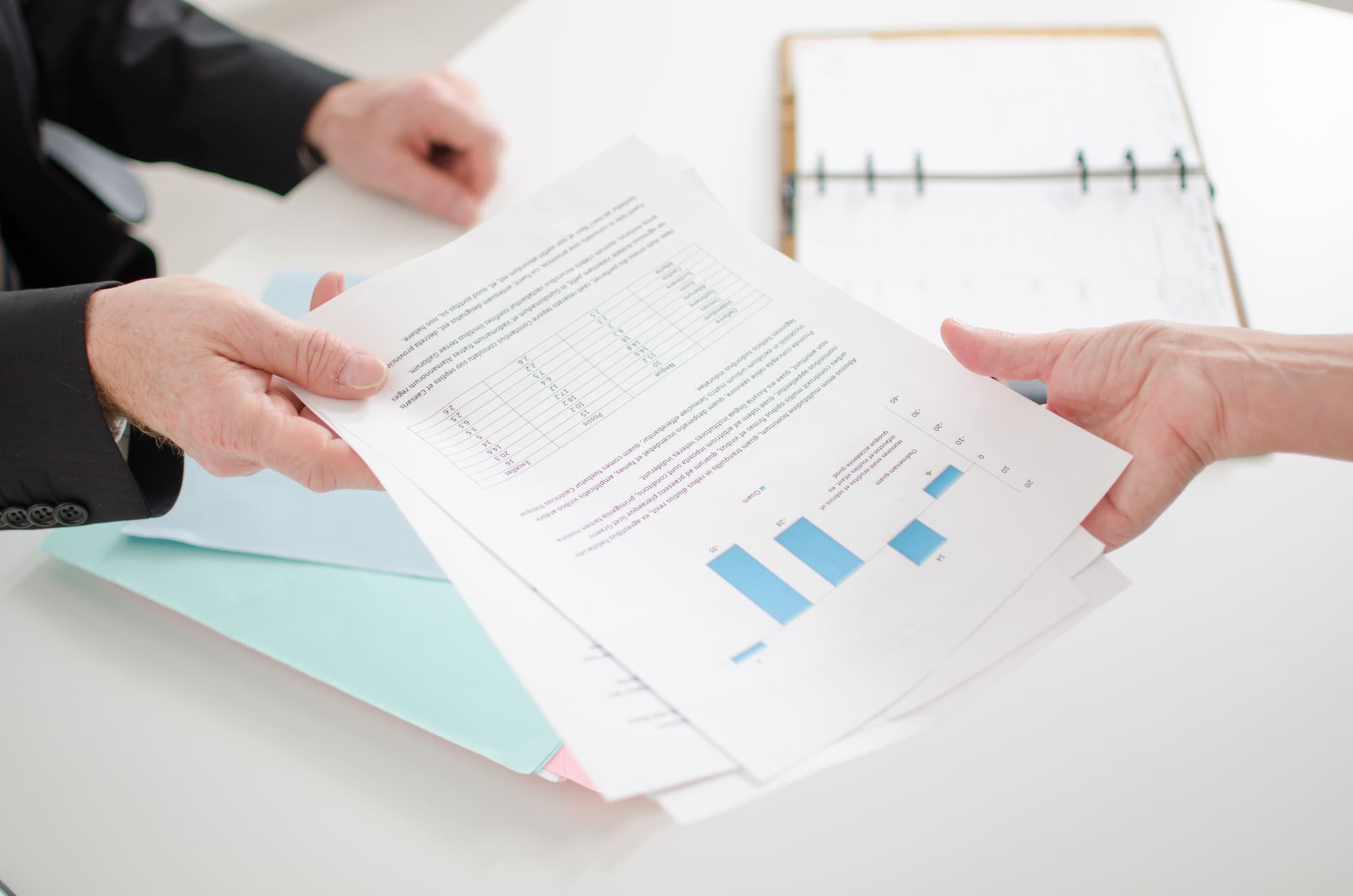 引越し時の追加サポート資料をイメージする、グラフや文字が書かれた書類を交換する二人の手