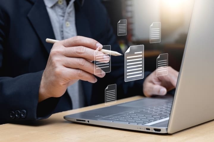 不動産DXの活用をイメージする、ノートパソコンで作業する手とデジタル書類